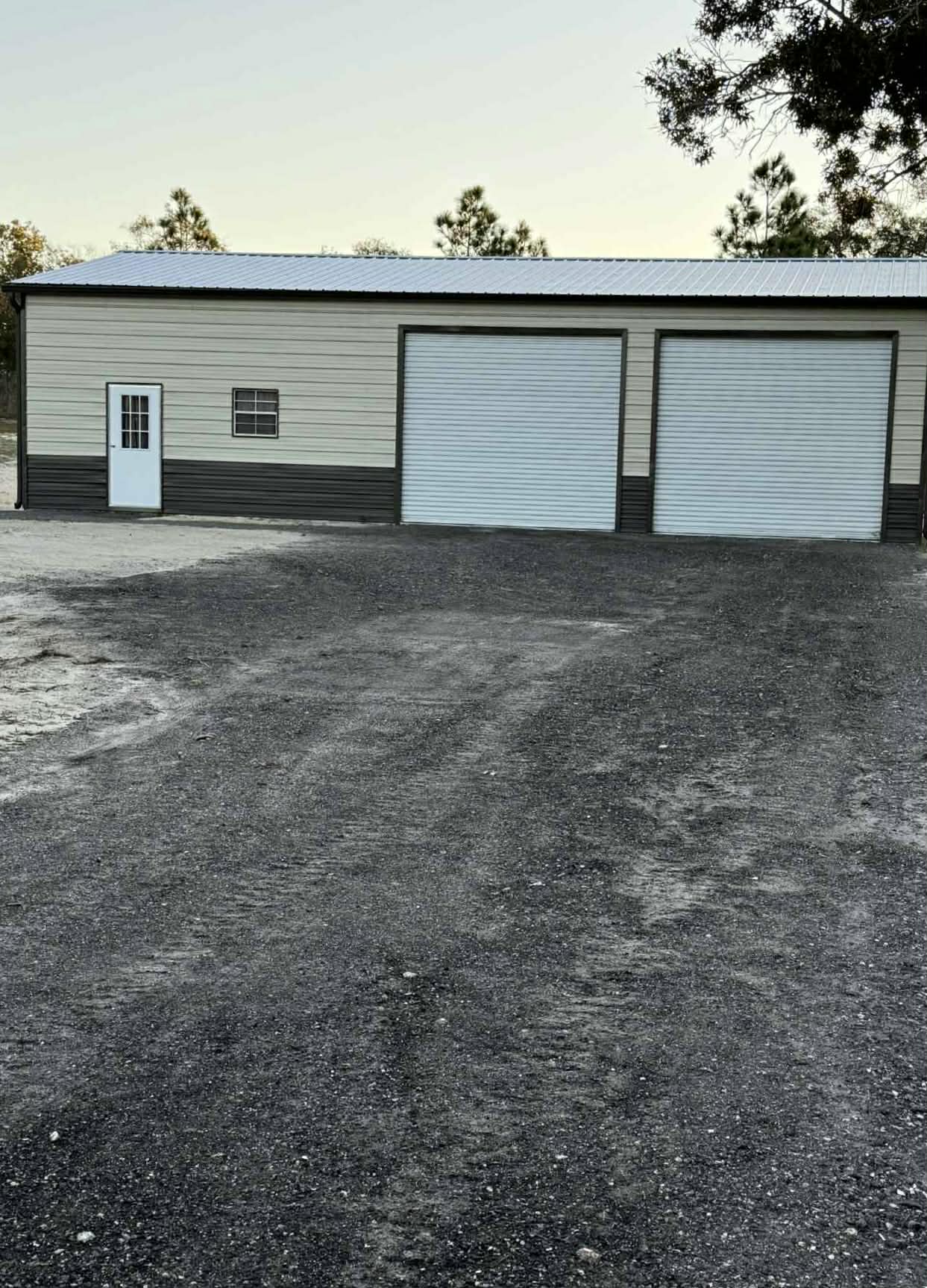 Front view of tan metal garage with gravel driveway